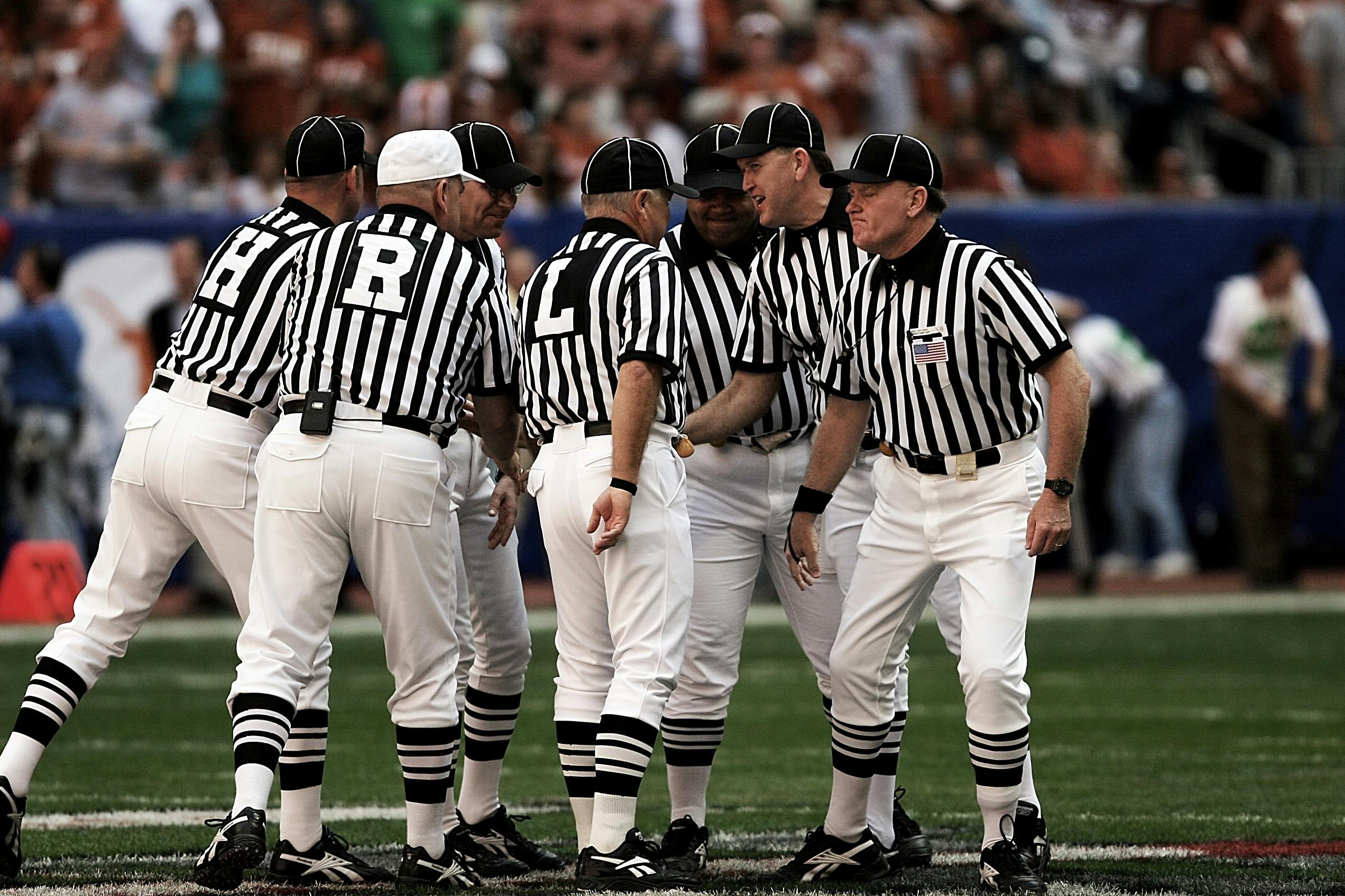Team of referees discussing a play during a football game in a vibrant stadium.